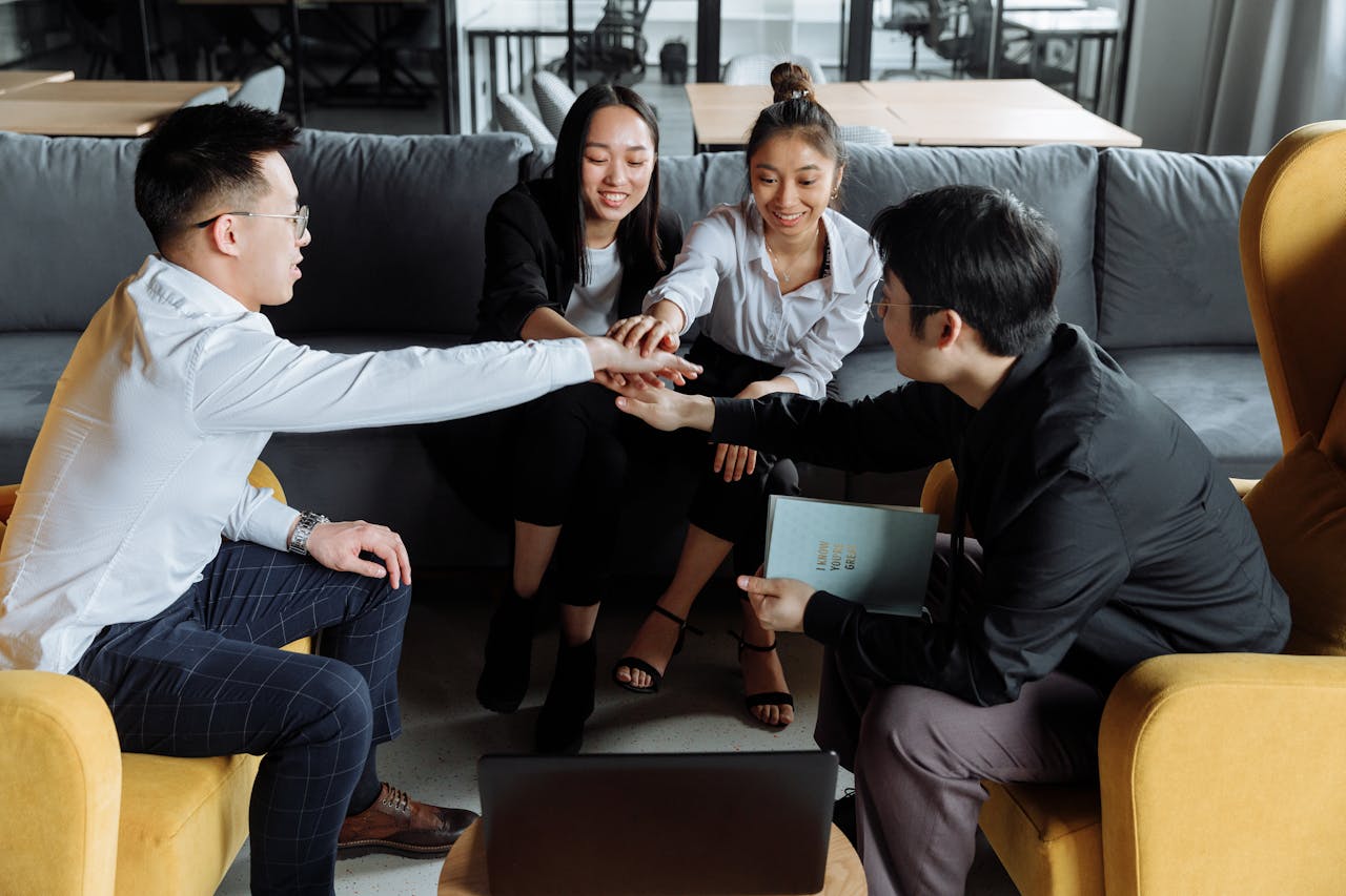 A Group Of Four Young Professionals Putting Their Hands Together In An Office Setting